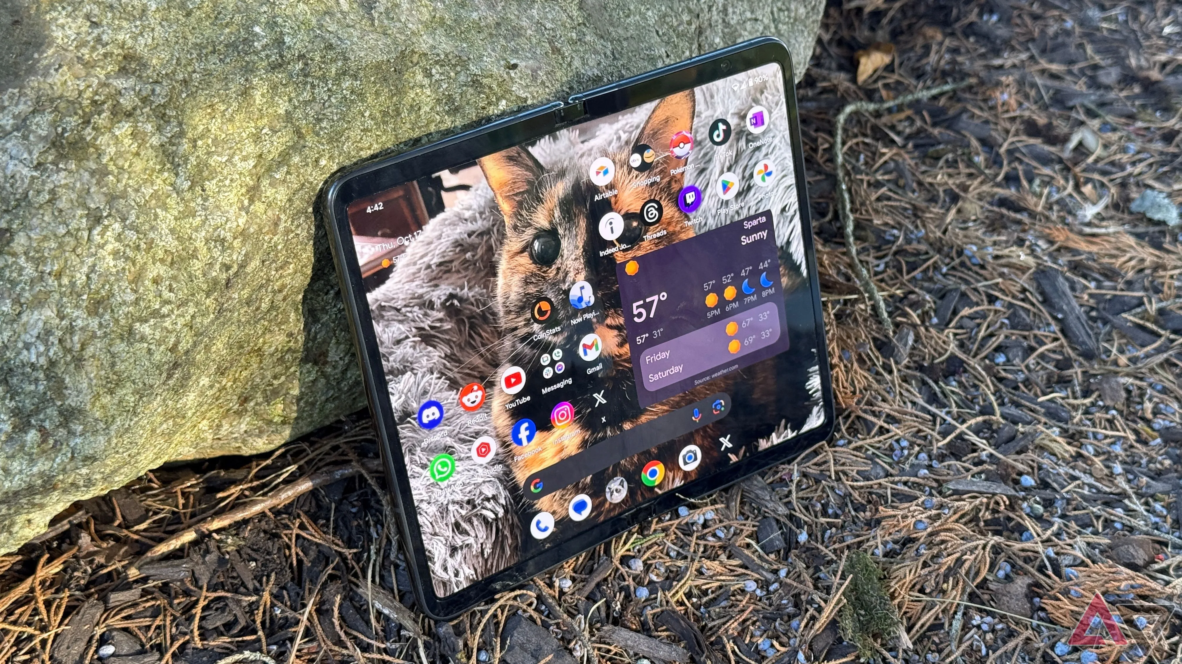 Điện thoại gập Google Pixel Fold màu đen đặt nghiêng tựa vào một tảng đá ngoài trời.
