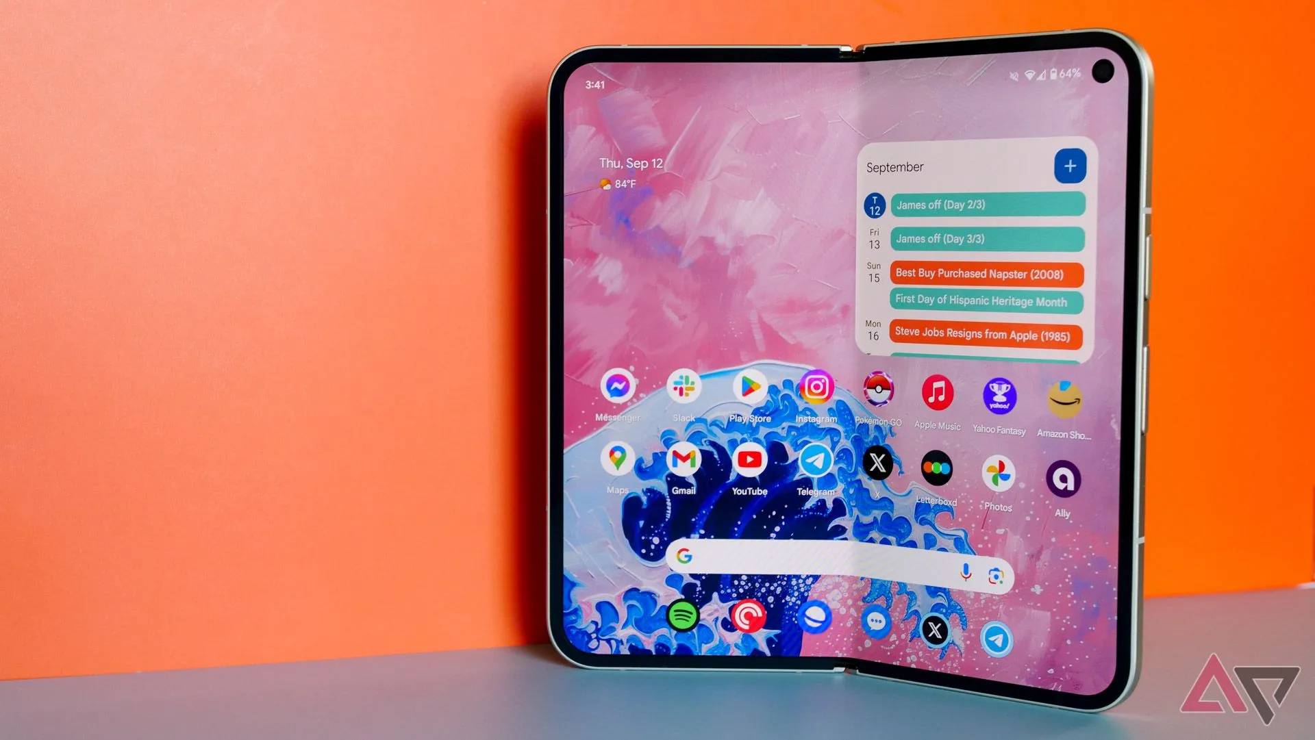 Điện thoại Google Pixel 9 Pro Fold đang mở ra, đặt trước phông nền màu cam.