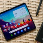 Điện thoại Google Pixel Fold màu đen đặt trên bàn mây tre đan cùng sổ tay và bút, gợi ý về khả năng làm việc.