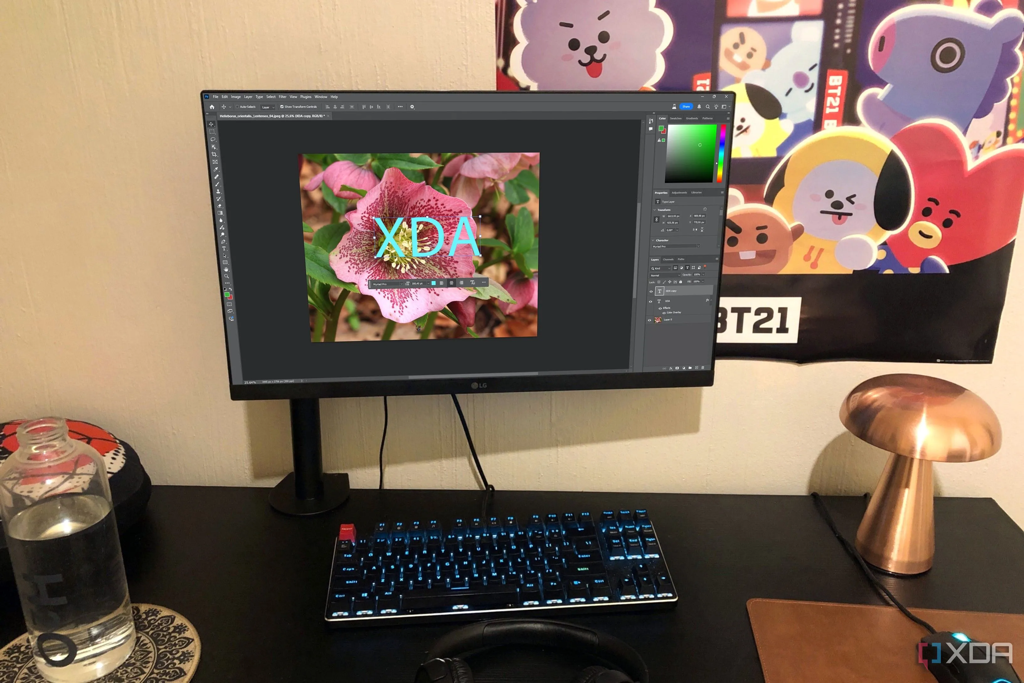 Giao diện phần mềm Photoshop trên máy tính để bàn với hiệu ứng màu hồng và các vật dụng trang trí như đèn, chai nước, poster