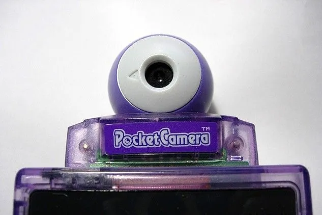 Máy ảnh Game Boy Camera màu tím gắn trên một chiếc Game Boy màu tím, thể hiện khả năng chụp ảnh độc đáo.