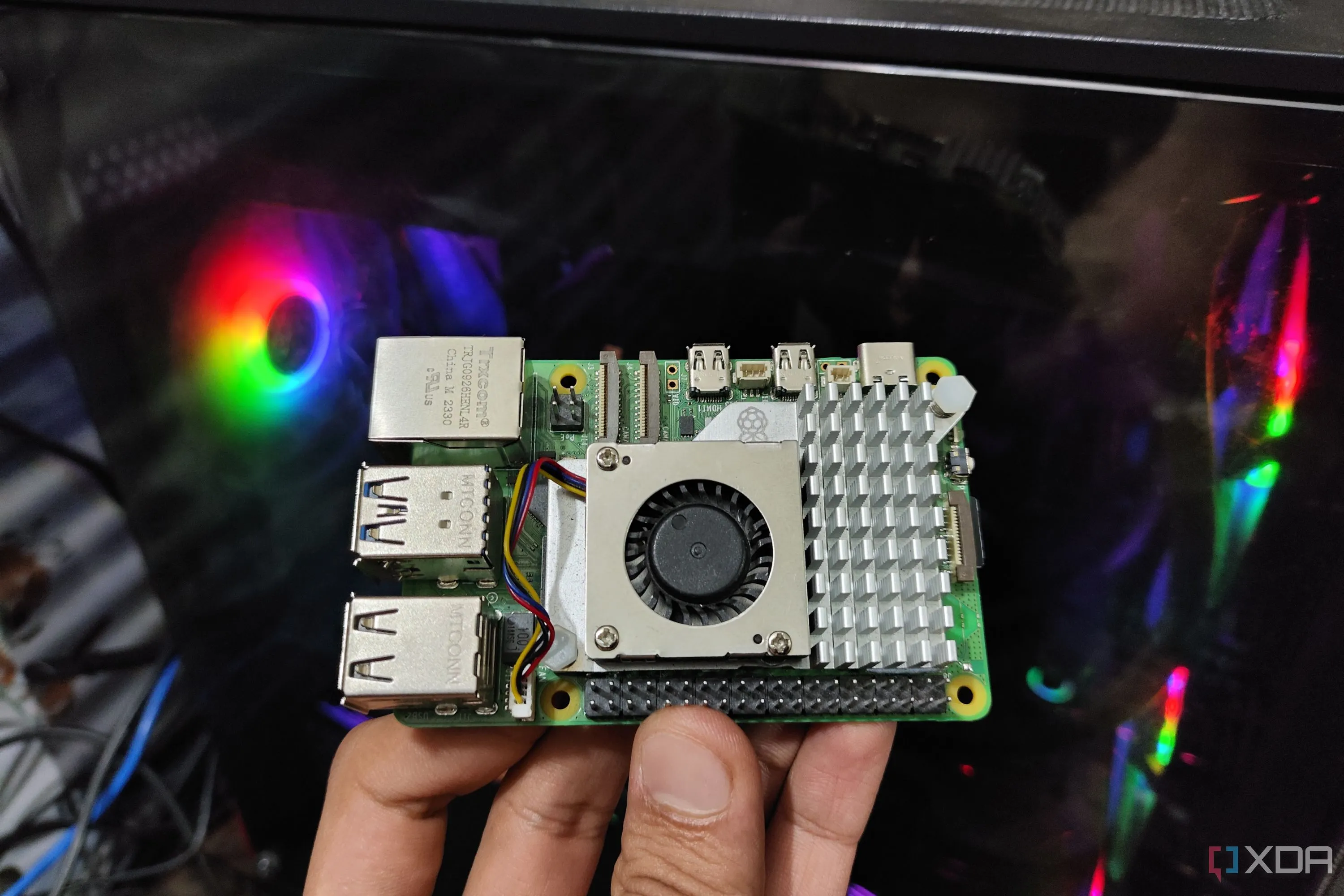 Một chiếc Raspberry Pi 5 đang được cầm trước máy tính, thể hiện tiềm năng biến thiết bị nhỏ gọn này thành máy chủ văn phòng tự host.
