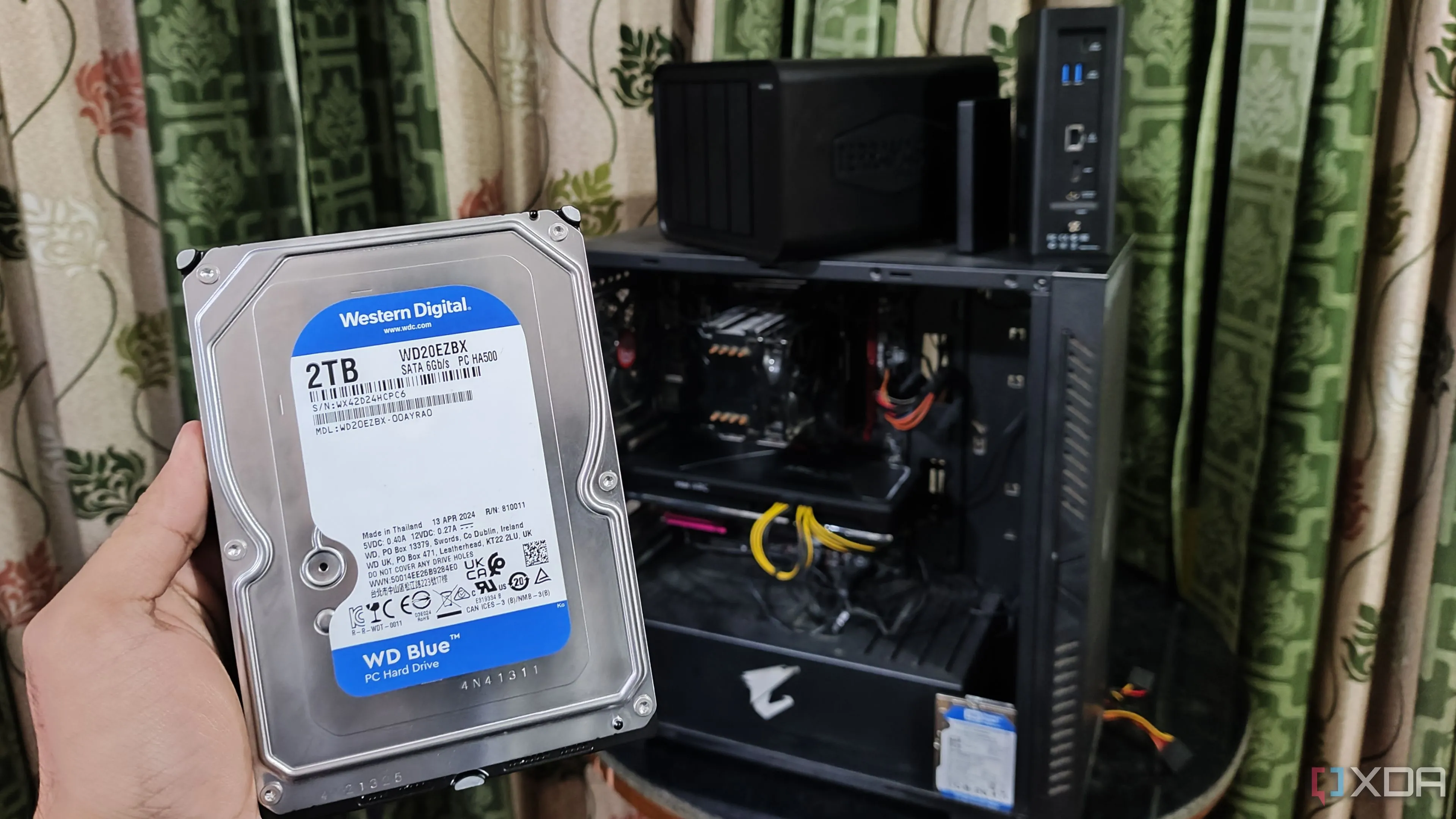 Một người đang cầm ổ HDD trước PC và hai thiết bị NAS TerraMaster