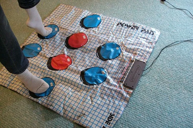 Một người phụ nữ đang đứng trên NES Power Pad màu xám, chơi game thể dục với tay cầm Nintendo.