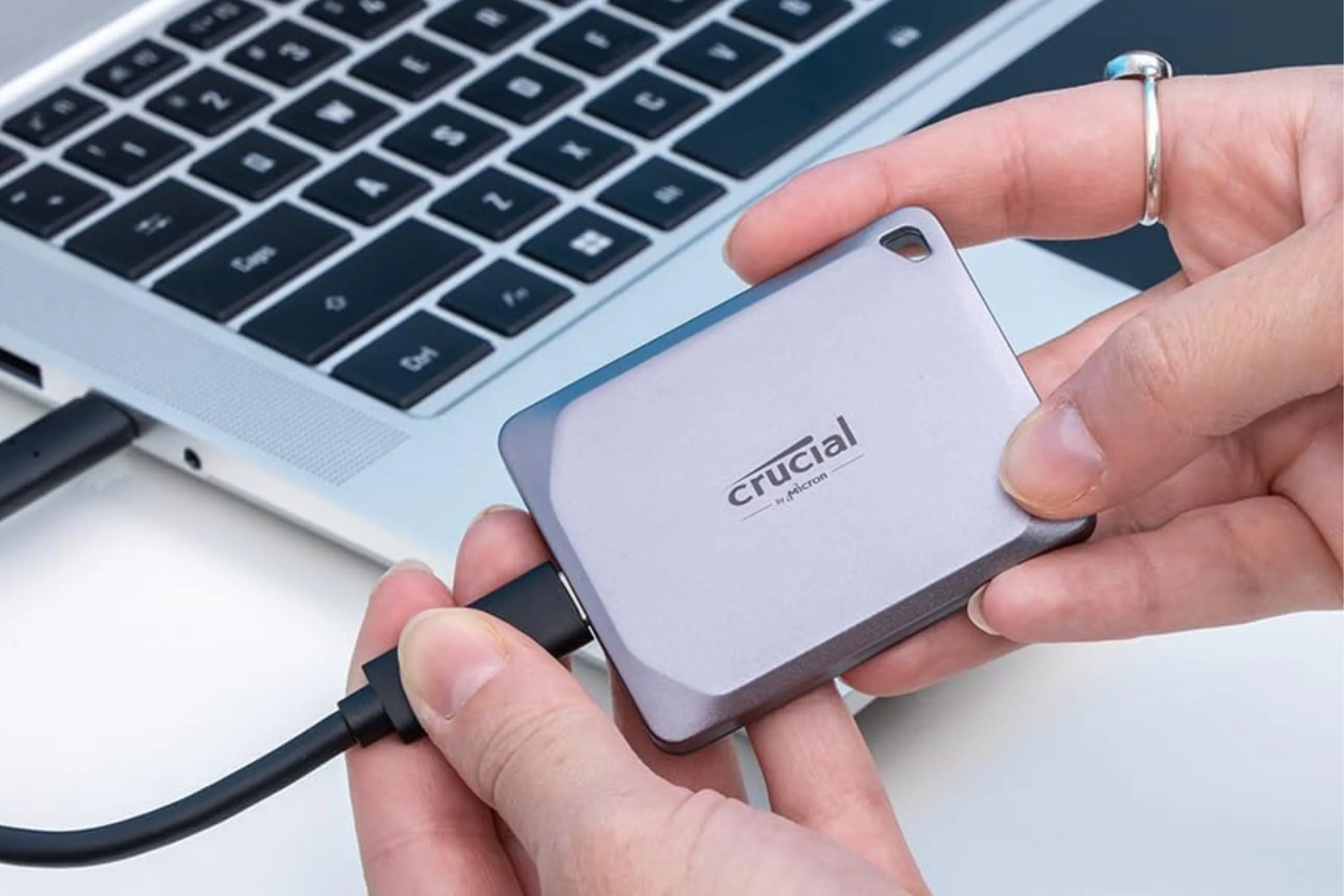 Người dùng cầm ổ cứng Crucial X9 Pro 1TB cạnh máy tính, minh họa tính di động